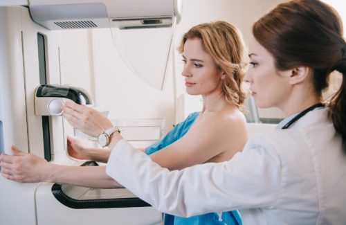 attentive radiographer adjusting x-ray machine for mammography test while standing near patient