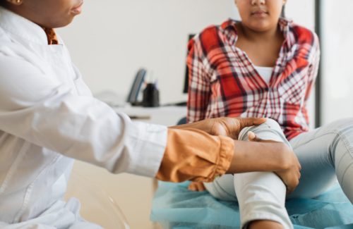 Close up of afro woman doctor examining patient with knee problems in clinic. Mixed race 10-aged