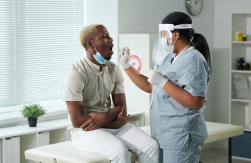 Young African male patient with open mouth being tested for covid by clinician